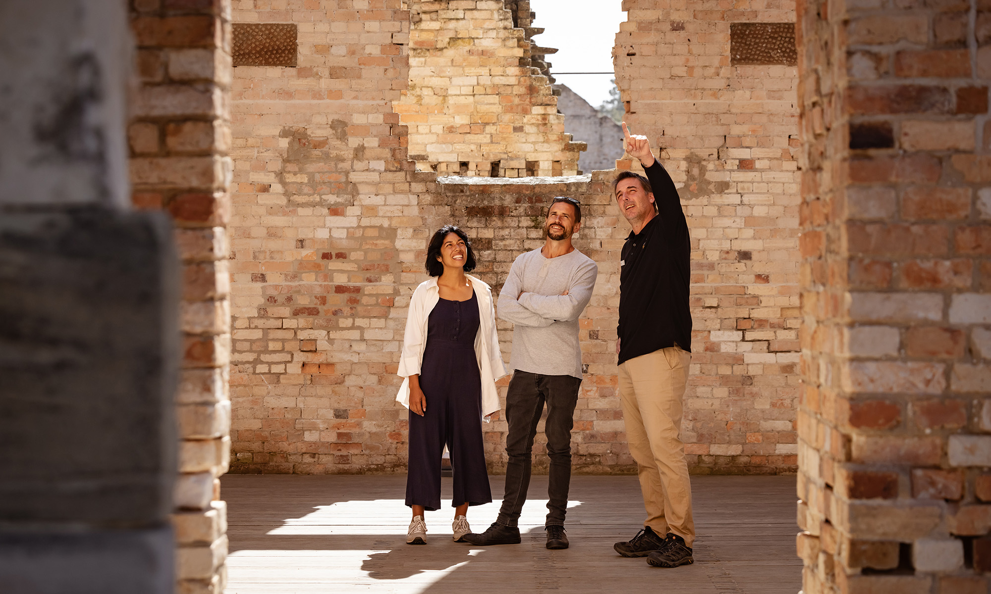 Three people stand looking around among half-crumbling brick walls.